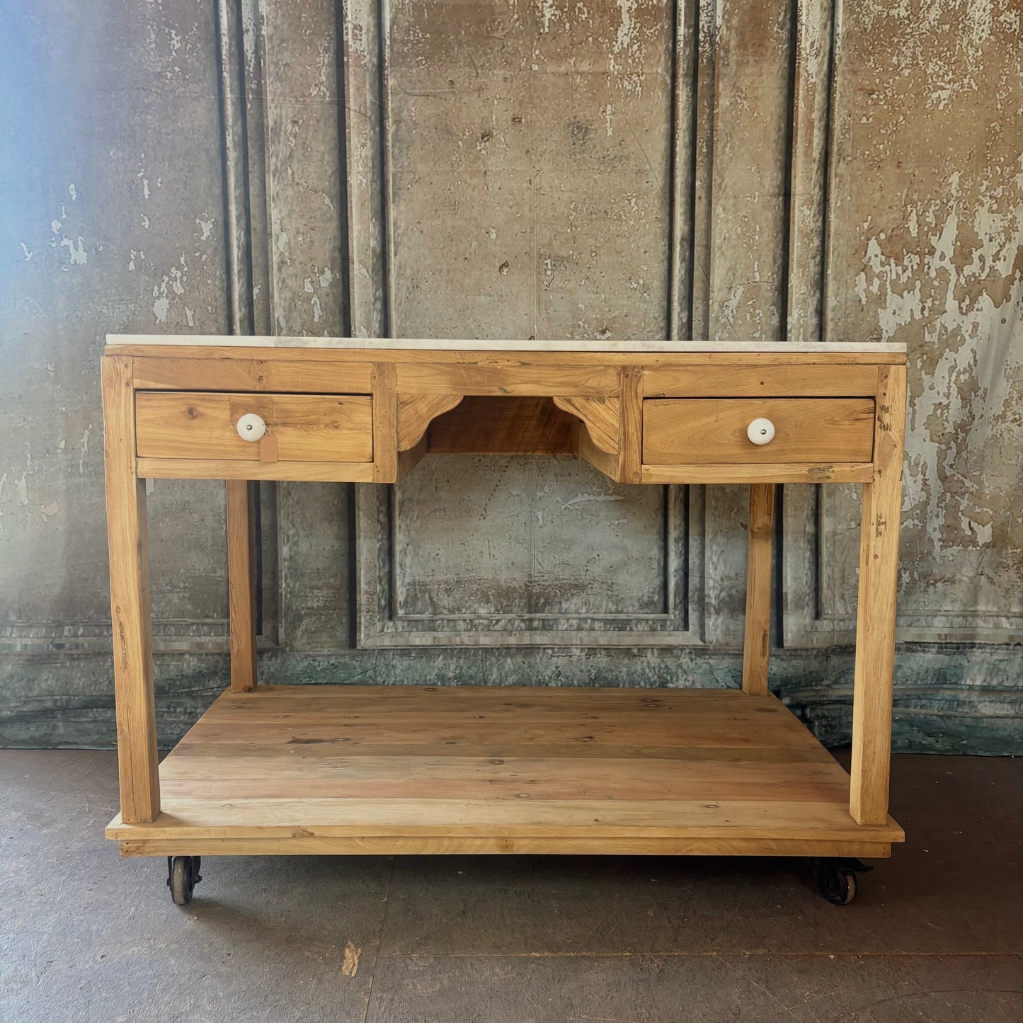 Wooden console table with two drawers and a shelf against a textured wall.